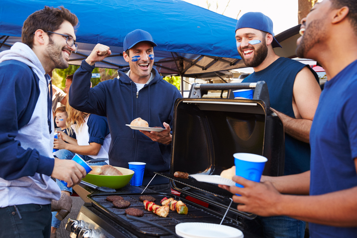 College students smiling and talking around a grill during a college football tailgate.